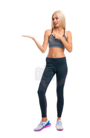 Foto de Cuerpo completo de mujer rubia en ropa de fitness mostrando o dando algo, aislado sobre fondo blanco. Deportes individuales y concepto de ejercicio. - Imagen libre de derechos