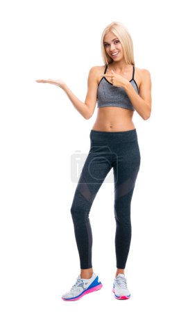 Foto de Cuerpo completo de mujer rubia en ropa de fitness mostrando o dando algo, aislado sobre fondo blanco. Deportes individuales y concepto de ejercicio. - Imagen libre de derechos