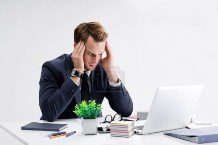 Photo for Stressed, tired businessman or heaving headache, holding his head, in black suit, working with laptop computer at office. Business fall, job and education concept. - Royalty Free Image