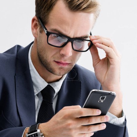 Téléchargez les photos : Homme d'affaires sérieux en lunettes et costume noir à l'aide d'un téléphone portable. Succès dans le concept d'entreprise, d'emploi et d'éducation. - en image libre de droit