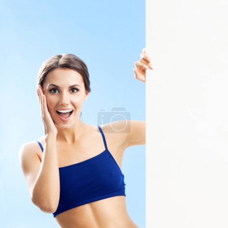Foto de Mujer joven alegre en ropa de fitness que muestra letrero en blanco o espacio de copia, sobre fondo azul - Imagen libre de derechos