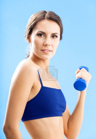 Foto de Mujer alegre en ropa de fitness haciendo ejercicio con mancuerna, sobre fondo azul - Imagen libre de derechos