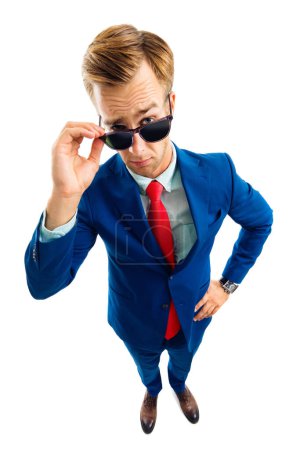 Are you seriously?! Full body portrait of funny skeptic young businessman in blue confident suit and red tie, looking through sunglasses, top angle view shot, isolated against white background. Business concept.