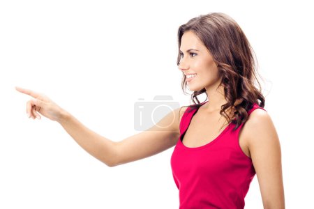 Téléchargez les photos : Vue du profil de la belle jeune femme souriante en vêtements rouges intelligents décontractés, montrant l'espace de copie, imaginaire visuel ou quelque chose, ou en appuyant sur un bouton virtuel, isolé sur fond blanc - en image libre de droit