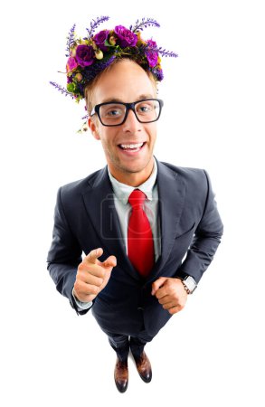 Photo for Full body portrait of funny happy businessman in glasses, confident suit, red tie and wreath of wildflowers on her head, pointing on you, top angle view shot, isolated over white background. - Royalty Free Image