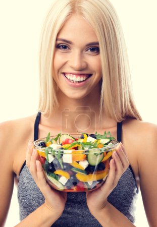 Photo for Woman in sportswear with plate of salad, isolated over yellow background. Young sporty blond model at studio shot. Health, beauty and fitness concept. - Royalty Free Image