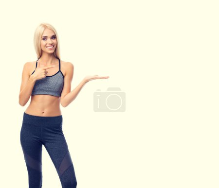 Photo for Woman in fitness wear showing or giving something, with copyspace area for slogan or advertising text message, isolated over yellow background. Individual sports and exercising concept. - Royalty Free Image
