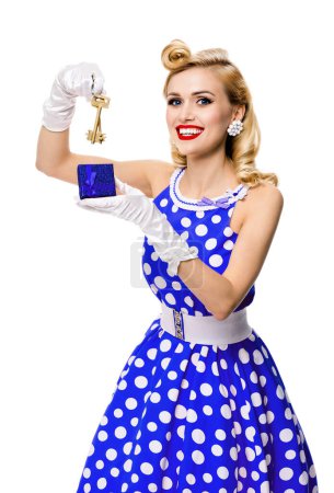 Téléchargez les photos : Joyeux sourire femme blonde dans le style pin-up robe bleue à pois, montrant les clés de la nouvelle maison, isolé sur fond blanc. Modèle caucasien posant dans la mode rétro, concept vintage et immobilier. - en image libre de droit