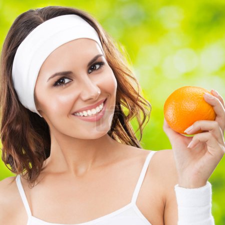 Téléchargez les photos : Portrait de jeune femme souriante heureuse en tenue de fitness avec orange, à l'extérieur - en image libre de droit
