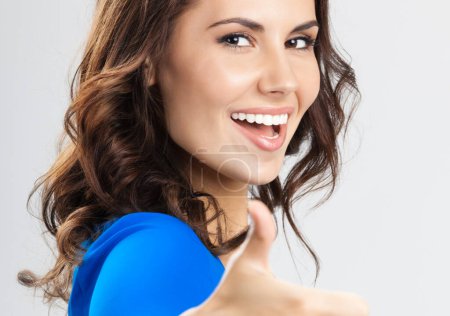 Téléchargez les photos : Portrait de jeune femme souriante heureuse montrant les pouces vers le haut geste, sur fond gris - en image libre de droit