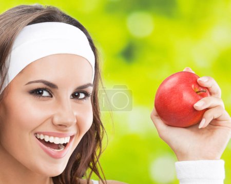 Téléchargez les photos : Portrait de jeune femme souriante heureuse en tenue de fitness avec pomme, à l'extérieur - en image libre de droit