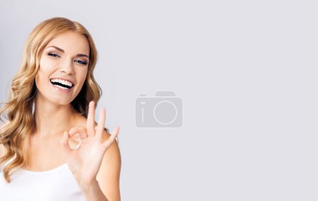 Foto de Retrato de una joven mujer rubia sonriente feliz mostrando un gesto correcto, con área de espacio libre para texto, eslogan o mensaje publicitario, sobre fondo gris - Imagen libre de derechos