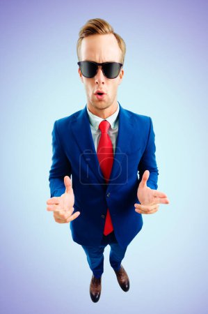 Téléchargez les photos : I am cool! Portrait of funny young businessman in sunglasses, confident suit and red tie, top angle view shot, on blue background. Business concept. - en image libre de droit