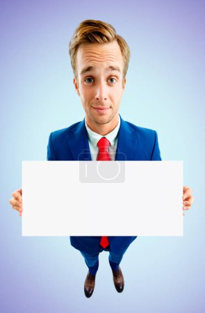 Photo for Businessman in confident suit and red tie, showing blank signboard with copyspace area for advertising text or slogan, top angle view shot, on blue background. Business concept. - Royalty Free Image