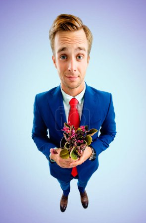 Porträt eines lustigen jungen Geschäftsmannes mit Brille, selbstbewusstem Anzug und roter Krawatte, Blumentopf mit Blumen in der Hand, Aufnahme aus der Vogelperspektive, auf blauem Hintergrund. Geschäftskonzept.