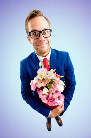 Porträt eines lustigen jungen Geschäftsmannes mit Brille, selbstbewusstem Anzug und roter Krawatte, Blumenstrauß in der Hand, Aufnahme aus der Vogelperspektive, auf blauem Hintergrund. Geschäftskonzept.