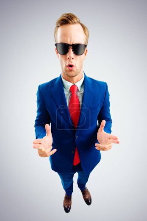 Téléchargez les photos : Je suis cool ! Portrait de drôle de jeune homme d'affaires en lunettes de soleil, costume bleu et cravate rouge, vue de dessus, sur fond gris. Concept d'entreprise. - en image libre de droit