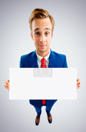 Téléchargez les photos : Homme d'affaires en costume bleu et cravate rouge, montrant l'enseigne vierge avec la zone de copyspace pour le texte ou le slogan de publicité, vue d'angle supérieur, au-dessus du fond gris. Concept d'entreprise. - en image libre de droit
