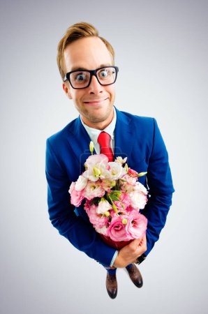 Téléchargez les photos : Portrait de jeune homme d'affaires drôle en lunettes, costume bleu et cravate rouge, tenant bouquet de fleurs, vue de dessus angle, sur fond gris. Concept d'entreprise. - en image libre de droit