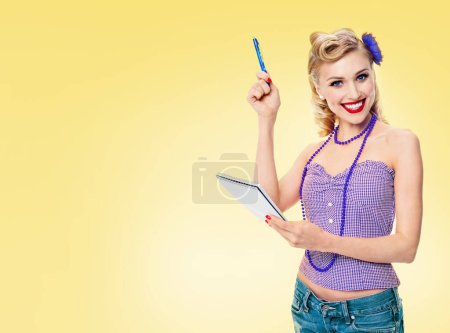 Photo for Happy smiling woman with notepad, in pin up style clothing, with copyspace area for slogan or advertising text message, on yellow background. Caucasian blond model in retro fashion and vintage concept. - Royalty Free Image
