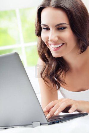 Téléchargez les photos : Joyeux jeune femme utilisant un ordinateur portable, à la maison - en image libre de droit
