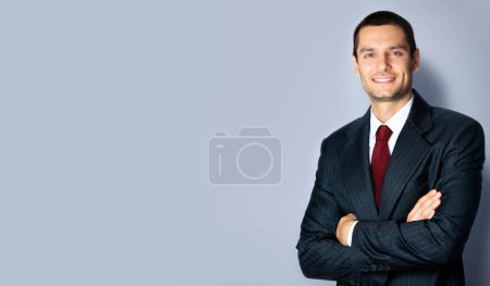 Photo for Portrait of confident young businessman in black suit and red tie, with crossed arms pose, empty copy space place for some text, advertising or slogan, standing over grey background - Royalty Free Image