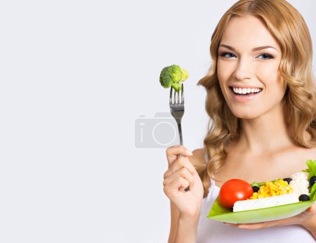 Photo for Smiling young beautiful woman with healthy vegetarian salad, over gray background. Copyspace blank area for some advertise, slogan or text. - Royalty Free Image