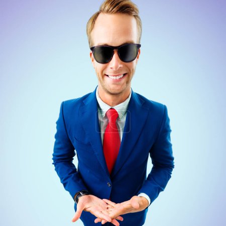 Foto de ¿Y qué? Joven empresario divertido en gafas de sol, traje de confianza y corbata roja, sobre fondo azul. Concepto empresarial. - Imagen libre de derechos