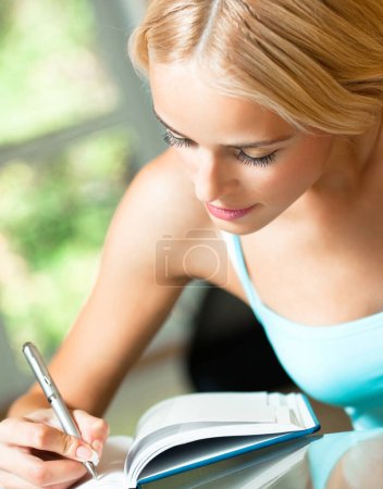 Téléchargez les photos : Jeune femme étudiant avec ordinateur portable ou organisateur, à l'intérieur - en image libre de droit