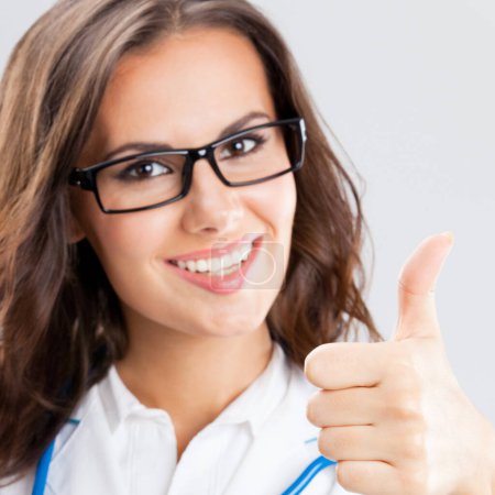 Female doctor with thumbs up gesture, over grey background