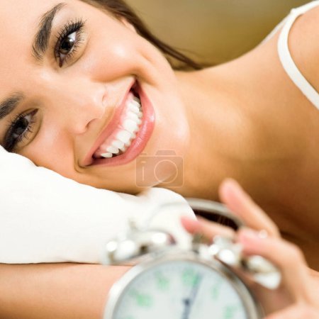 Téléchargez les photos : Jeune femme avec réveil sur le lit - en image libre de droit
