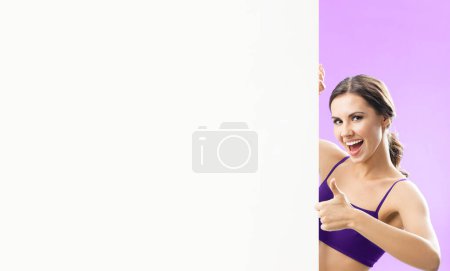 Photo for Young woman in fitness wear showing blank signboard with copyspace for some text, advertising or slogan, against pink background - Royalty Free Image
