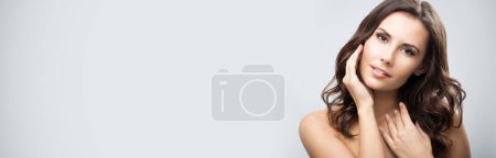 Téléchargez les photos : Portrait de belle jeune femme aux longs cheveux bouclés, sur fond gris - en image libre de droit