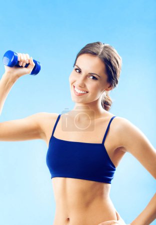 Foto de Retrato de mujer joven en ropa de fitness haciendo ejercicio con mancuerna, sobre fondo azul - Imagen libre de derechos