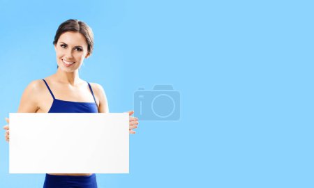 Foto de Retrato de mujer feliz en ropa de fitness mostrando letrero en blanco o espacio de copia, sobre fondo azul - Imagen libre de derechos