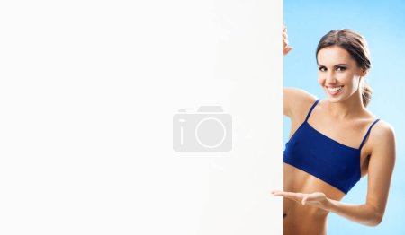 Photo for Portrait of happy woman in fitness wear showing blank signboard or copyspace, over blue background - Royalty Free Image