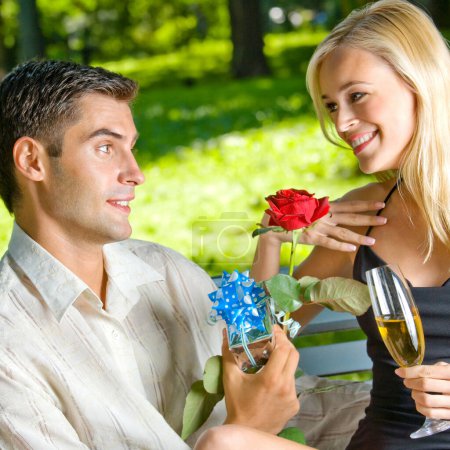 Foto de Joven feliz sonriente alegre pareja con regalos, rosa y champán, al aire libre - Imagen libre de derechos