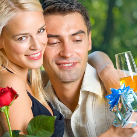 Foto de Joven feliz sonriente alegre pareja con regalos, rosa y champán, al aire libre - Imagen libre de derechos
