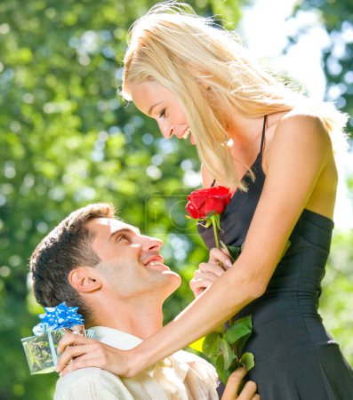 Téléchargez les photos : Jeune couple joyeux et souriant avec cadeaux, rosa et champagne, en plein air - en image libre de droit