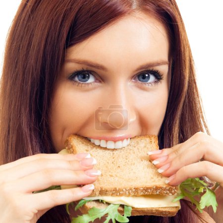 Téléchargez les photos : Portrait d'une jeune femme joyeuse mangeant un sandwich au fromage, isolée sur fond blanc - en image libre de droit