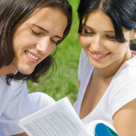 Téléchargez les photos : Jeune couple souriant heureux ou étudiants, lire un livre ensemble, en plein air - en image libre de droit