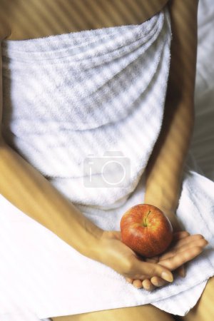 Téléchargez les photos : Une femme vêtue d'une serviette blanche tient une pomme rouge dans ses mains - en image libre de droit