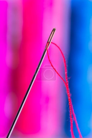 Téléchargez les photos : Vue rapprochée d'une aiguille avec fil rouge avec des bobines de fil de couleur différente sur le fond - en image libre de droit