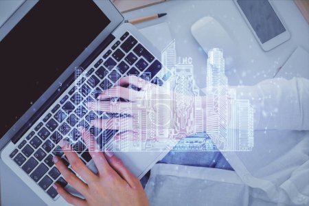 Double exposure of woman hands working on computer and buildings construction hologram drawing. Top View. smart city concept.