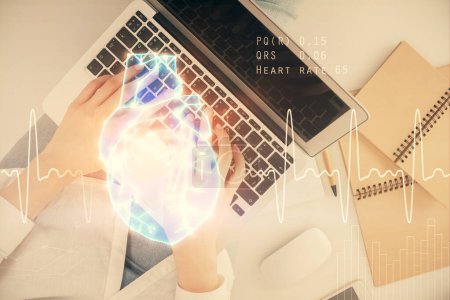 Foto de Doble exposición de las manos de las mujeres que trabajan en la computadora y el holograma del corazón dibujo. Vista superior. Concepto de Ciencias Médicas. - Imagen libre de derechos