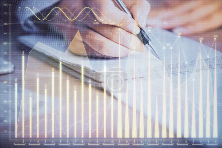 Photo for A woman hands writing information about stock market in notepad. Forex chart holograms in front. Concept of research. Multi exposure - Royalty Free Image