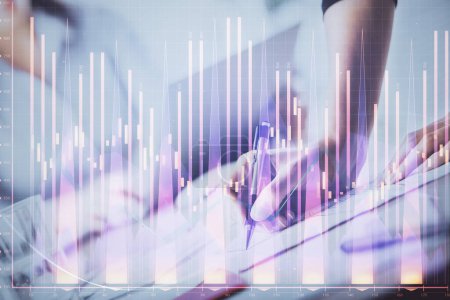 Photo for A woman hands writing information about stock market in notepad. Forex chart holograms in front. Concept of research. Double exposure - Royalty Free Image