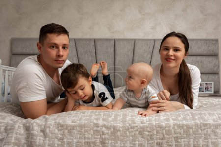 Photo for A big beautiful Ukrainian, emotional, cheerful family of dad, mom and two little sons is sitting on the bed, bright interior of the room. Family concept - Royalty Free Image