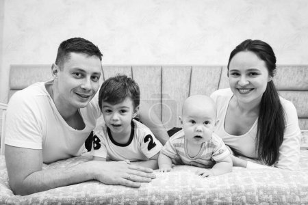 Photo for Young, emotional, cheerful, big family, mom, dad and sons lie on a big bed and look at the camera. - Royalty Free Image