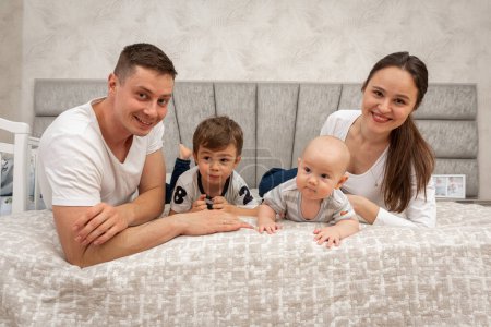 Photo for A big beautiful Ukrainian, emotional, cheerful family of dad, mom and two little sons is sitting on the bed, bright interior of the room. Family concept - Royalty Free Image